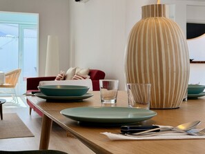 Een eettafel met borden, glazen en bestek, een gestreepte vaas, en een rode bank op de achtergrond.
