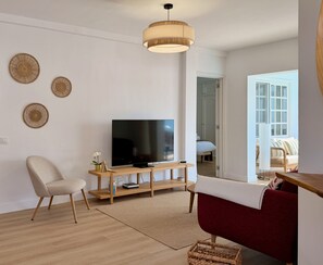 A modern living room with a flat-screen TV, a wooden entertainment unit, a red sofa, and a woven wall hanging. - CANARY LIGHT MASPALOMAS (Maspalomas)