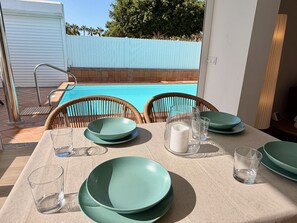 Un espace extérieur aménagé pour les repas, avec une piscine en arrière-plan.