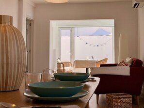 A modern living room with a dining area, featuring a red sofa, a wooden dining table, and a large window with curtains. - CANARY LIGHT MASPALOMAS (Maspalomas)