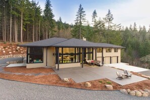 Une maison moderne dotée d’un grand patio, d’un espace salon extérieur abrité et offrant une vue sur une colline boisée.