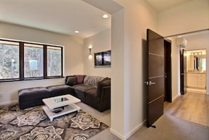 A modern living room with a sectional sofa, a coffee table, and a large window. - Phato's Retreat - Luxury Home, Hot Tub, Stunning Views (White Salmon)