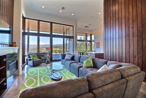 Un salon moderne avec un canapé d’angle, une table basse en verre et une vue sur l’extérieur.