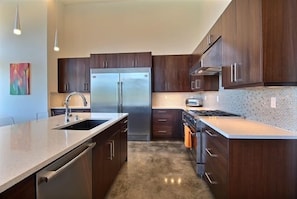 A modern kitchen with dark wood cabinets, stainless steel appliances, and a granite countertop. - Phato's Retreat - Luxury Home, Hot Tub, Stunning Views (White Salmon)