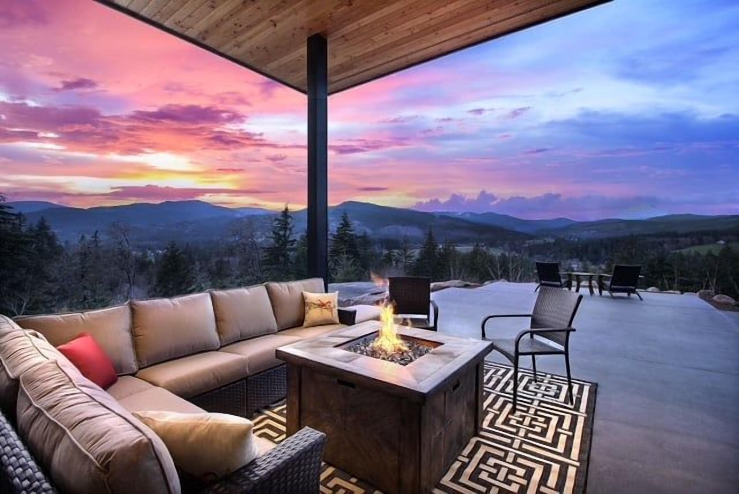 An outdoor seating area with a fire pit, a sofa, and chairs, overlooking a mountainous landscape.