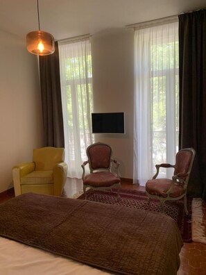 A hotel room with a bed, two chairs, a television on the wall, and large windows with curtains. - G3334 - DRAGUIGNAN - City Break (DRAGUIGNAN)