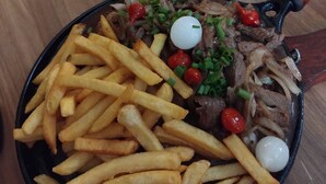 Un plato con carne, papas fritas y pan sobre una mesa.