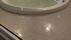 Una bañera redonda con panel de control, sobre un piso moteado, frente a una pared con diseño de mármol.