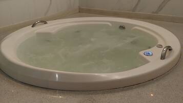 A round bathtub with a control panel, set on a speckled floor, against a wall with a marble pattern.