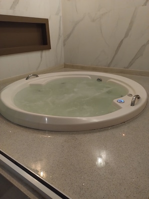 A round bathtub with a control panel, set on a speckled floor, against a wall with a marble pattern. - Vrbo Property (Manaus)