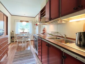 A kitchen with wooden cabinets, a stainless steel sink, and a dining area with a table and chairs. - 5 Person Holiday Home in Rockneby (Rockneby)