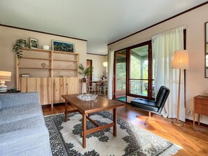 A living room with a wooden table, a sofa, a bookshelf, and a view through a glass door. - 5 Person Holiday Home in Rockneby (Rockneby)