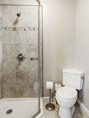 Un baño con cabina de ducha, inodoro y un rollo de papel higiénico en el suelo.