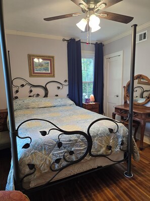 Un lit à baldaquin avec une couvre-lit à motifs, un ventilateur de plafond, une fenêtre avec des rideaux et un tableau encadré accroché au mur.
