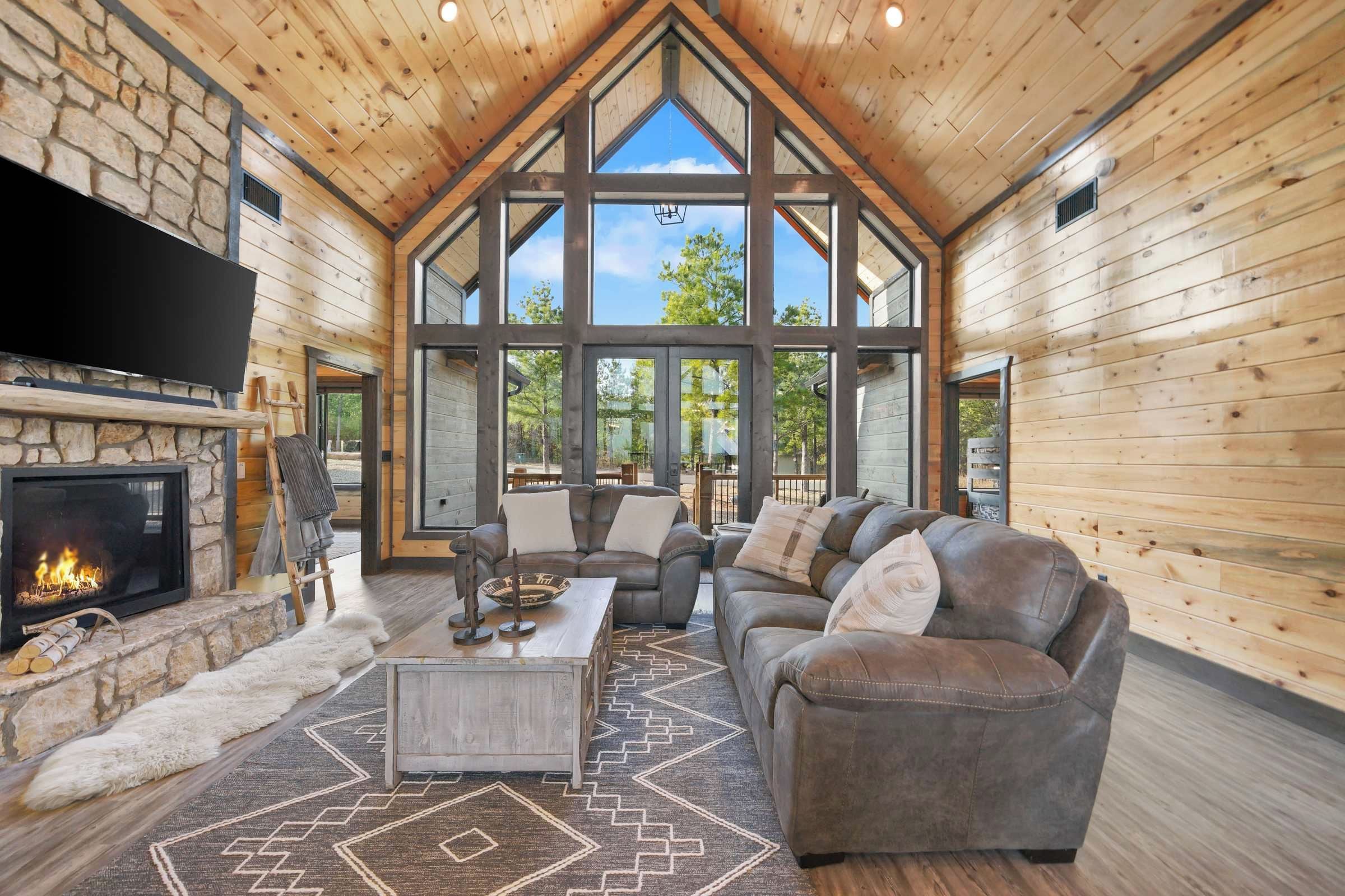 A log cabin interior with a fireplace, leather sofa, and large windows.