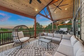 A covered outdoor area with a seating arrangement, a dining table, and a view of the landscape. - New! Cave Table Road! Fun Views! Hot Tub! Firepit! (Broken Bow)