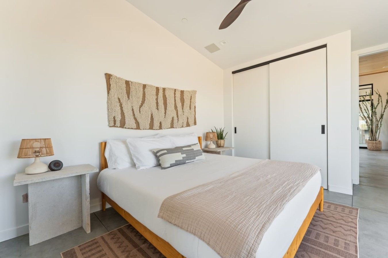 Une chambre à coucher moderne, avec un lit, des tables de chevet, une œuvre d’art accrochée au mur et un ventilateur de plafond.