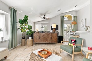 A modern living room with a herringbone wood cabinet, a green armchair, a small table with a bowl, and a decorative plant. - Beautiful Pool Home with Games Room Near Attractions (Kissimmee)
