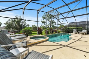 A pool area with lounge chairs and a hot tub, surrounded by a covered patio. - Beautiful Pool Home with Games Room Near Attractions (Kissimmee)