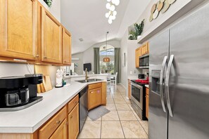 A modern kitchen with wooden cabinets, stainless steel appliances, and a central island. - Beautiful Pool Home with Games Room Near Attractions (Kissimmee)