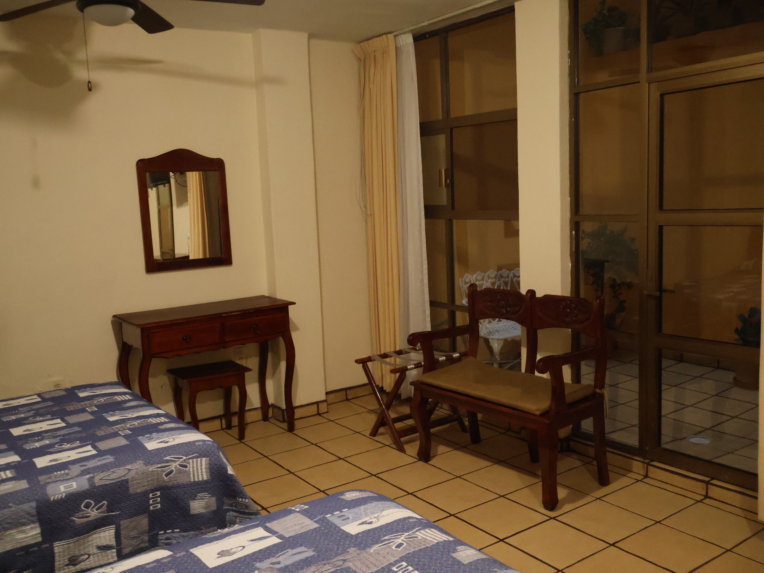 Una habitación con cama, escritorio, silla, espejo y puerta corrediza de vidrio.