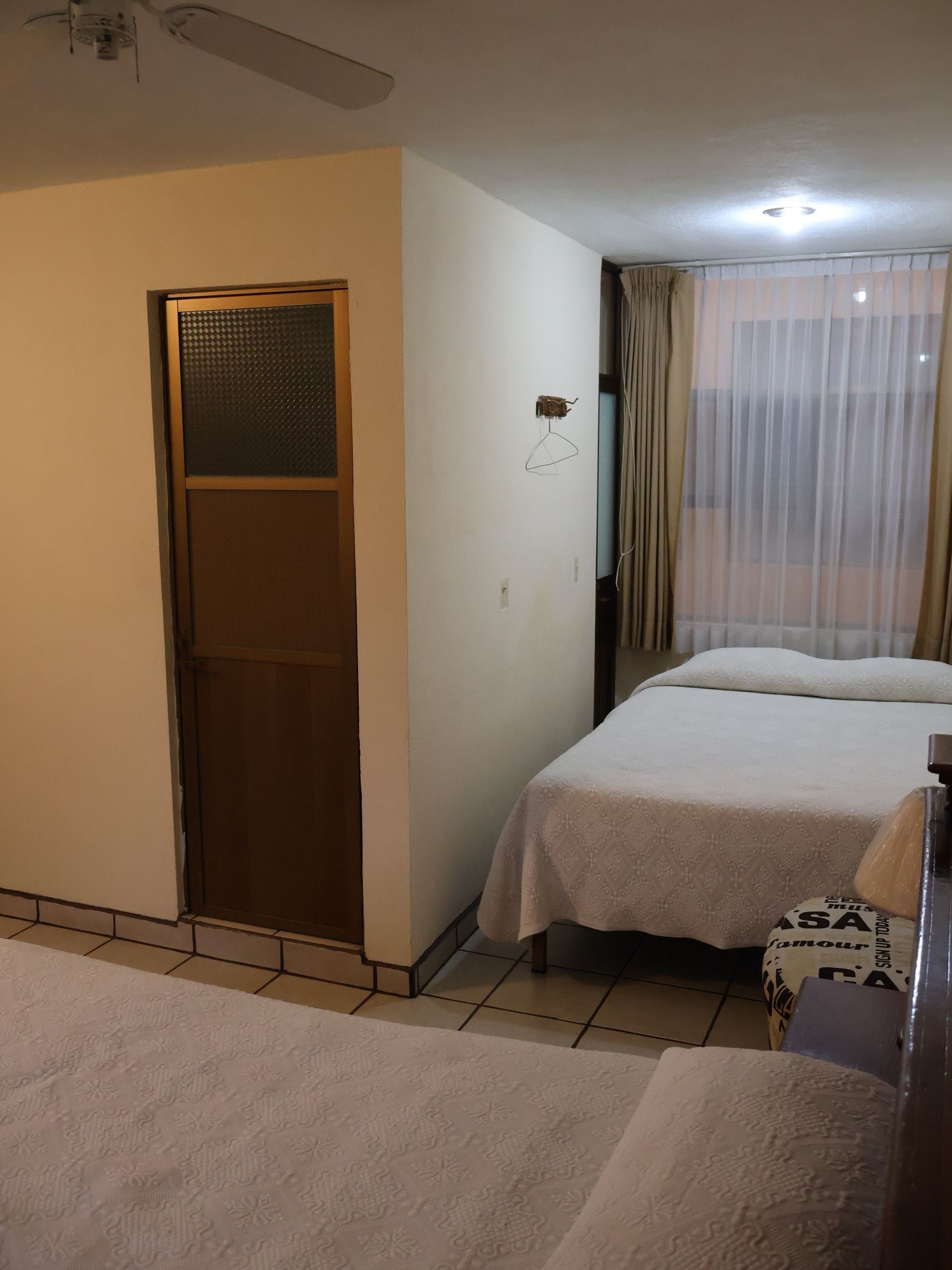 Habitación de hotel con dos camas, un armario, una mesita y un ventanal con cortinas.