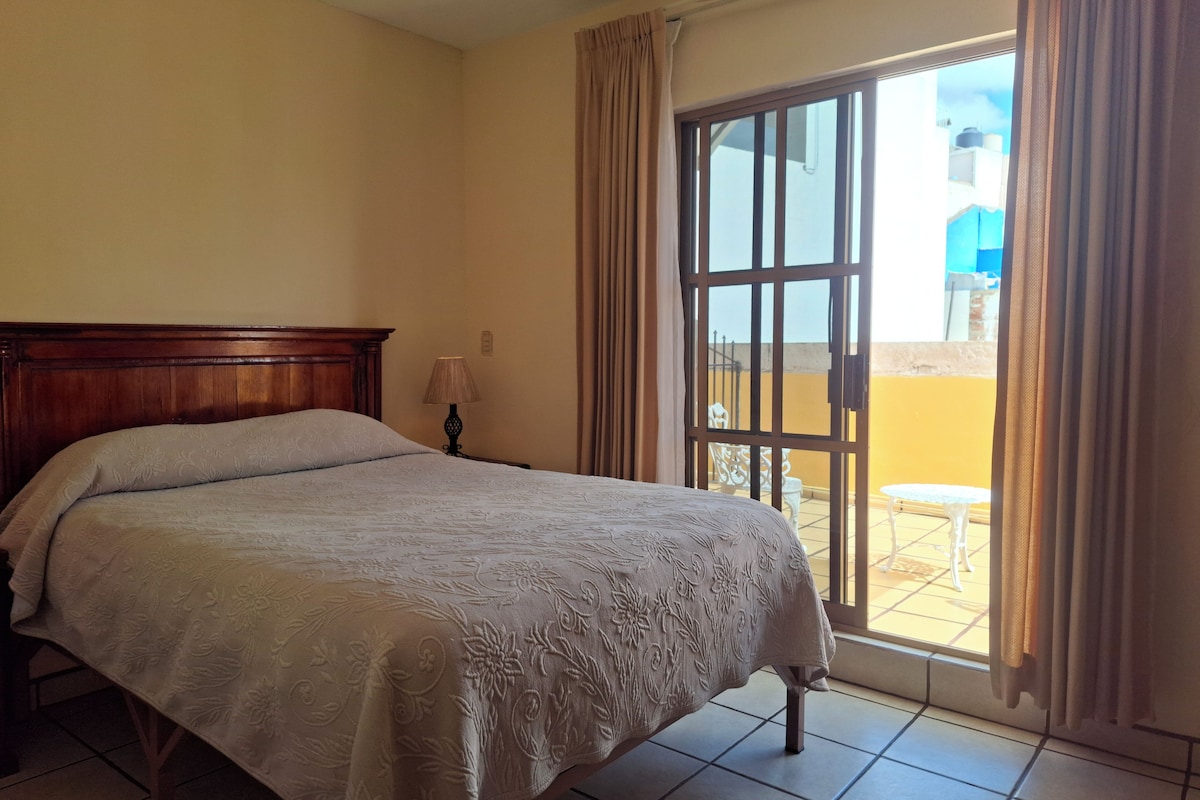 Un dormitorio con cama, mesita de noche, lámpara y vistas a un área exterior por una puerta corrediza.
