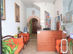 A reception area with a wooden desk, orange seating, and a wall decorated with flags. - Hotel Casa Cortes (Zacatecas)