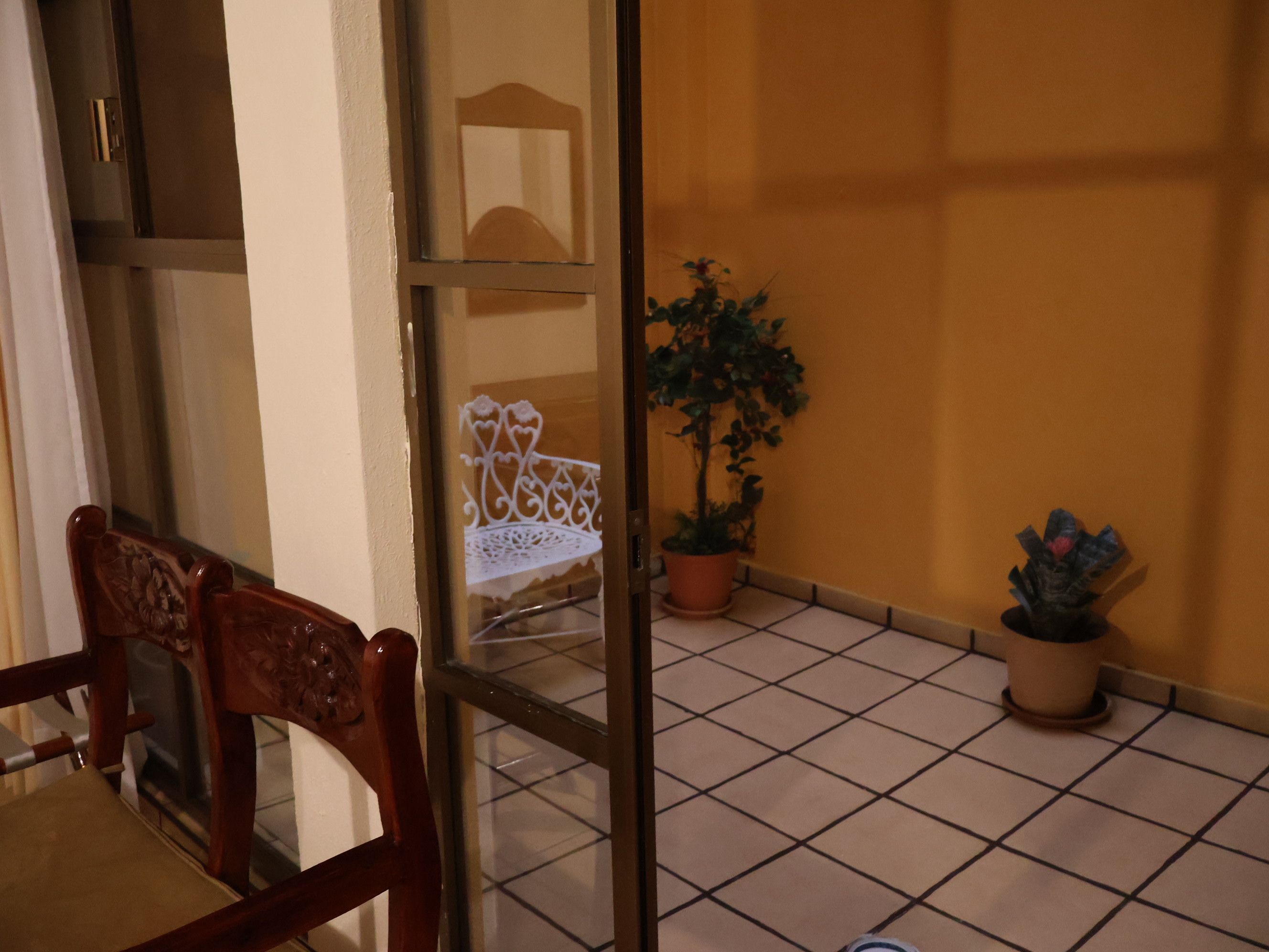 Una habitación con una silla de madera, una planta en maceta y un piso de baldosas.