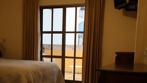 Ein Hotelzimmer mit einem Bett, einem Schreibtisch, einem an der Wand montierten Fernseher und einem Fenster mit Vorhängen.