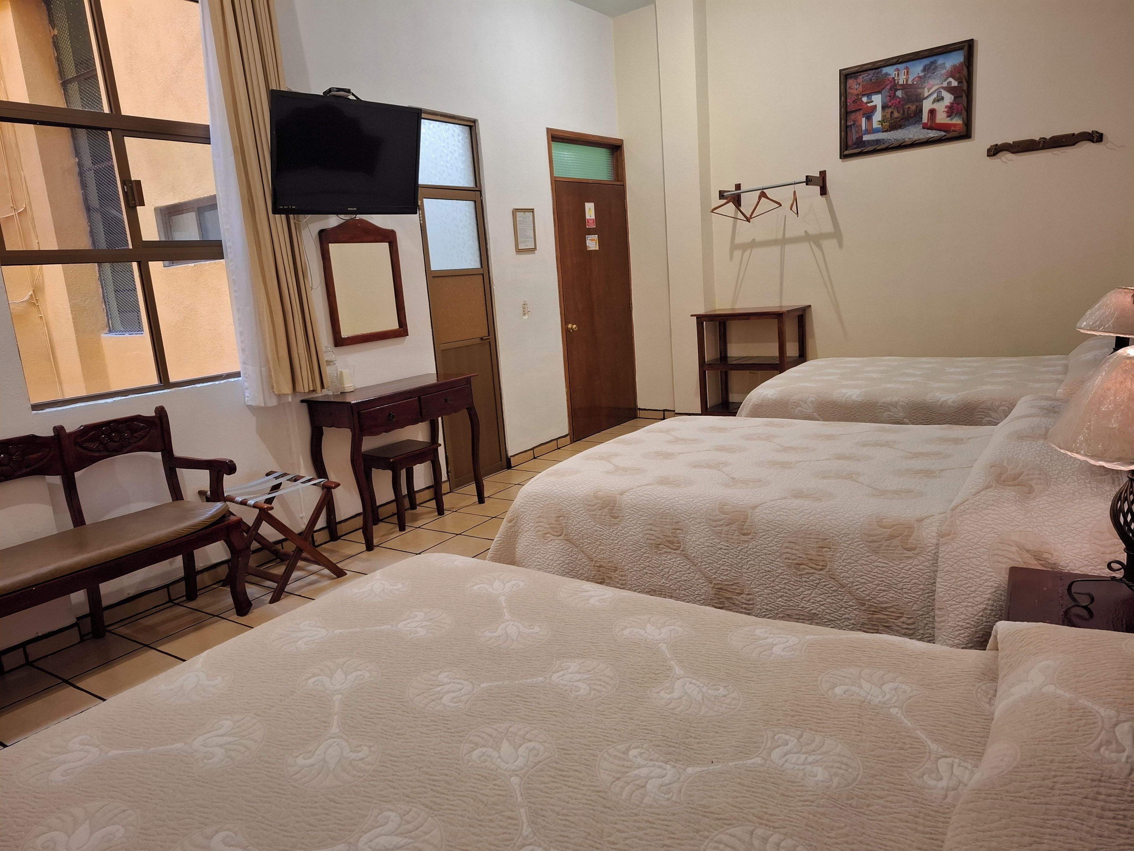 Habitación de hotel con cama, escritorio, silla, televisión, puerta y un cuadro en la pared.