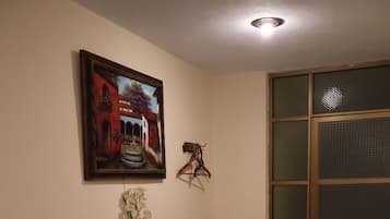 Una habitación con piso de baldosas, cómoda de madera, cuadro enmarco, planta en maceta, perchero colgante y puerta corrediza.