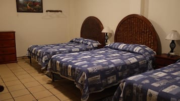 Un dormitorio con tres camas, un aparador de madera, un ventilador de techo, un cuadro colgado en la pared y una alfombra estampada.
