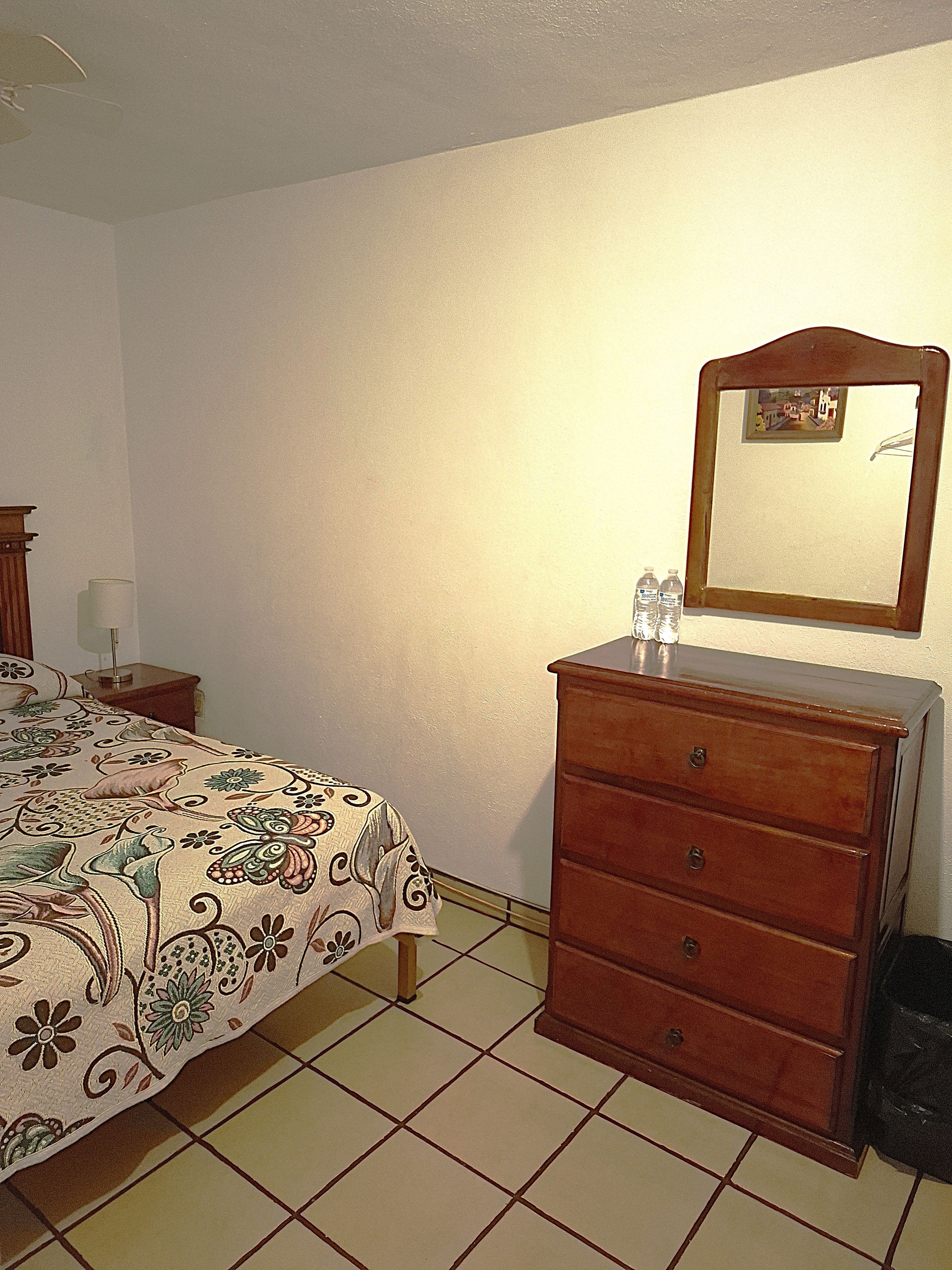 Un dormitorio con cama, tocador, espejo, mesita de noche y lámpara.