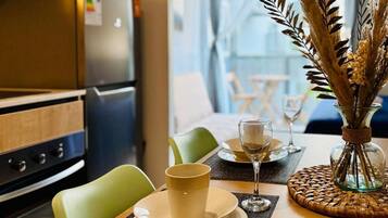 Un comedor con una mesa preparada para dos, un jarrón con plantas secas y una cocina al fondo.