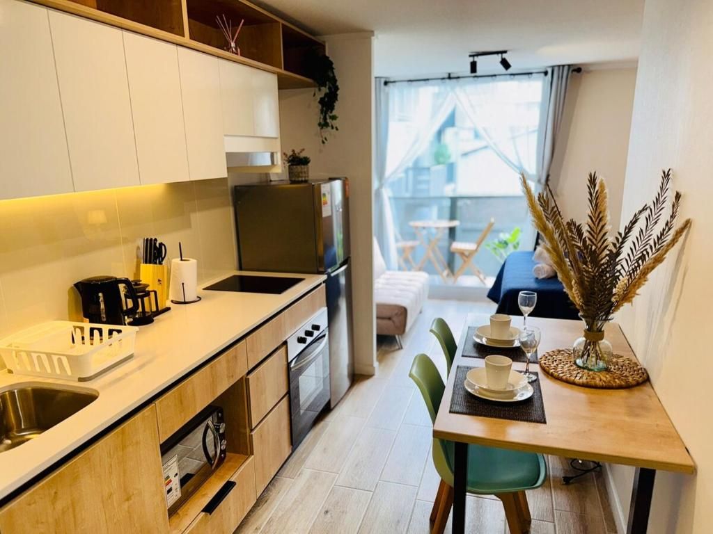 Cocina compacta con electrodomésticos modernos, comedor con una mesa para dos y vista al exterior a través de un ventanal amplio.