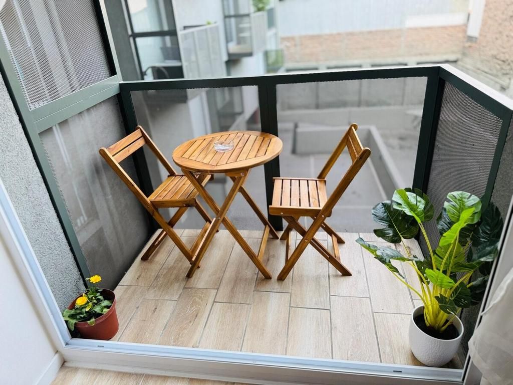Un pequeño balcón con una mesa de madera y dos sillas, una planta en maceta y vista a la calle.