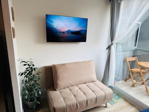 A room with a sofa, a potted plant, a flat-screen TV, and a dining area with chairs. - El mejor lugar - Estacionamiento - Wi-Fi (Santiago)