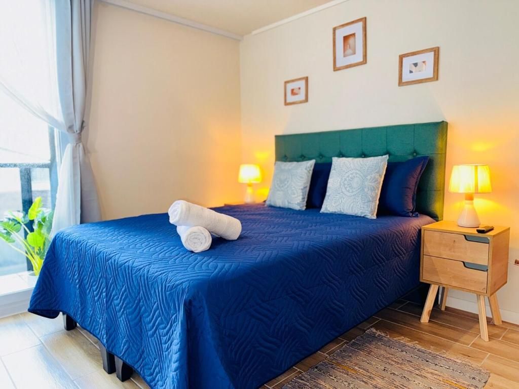 Una habitación de hotel con cama, lámparas de noche, mesita de noche y ventana con cortinas.