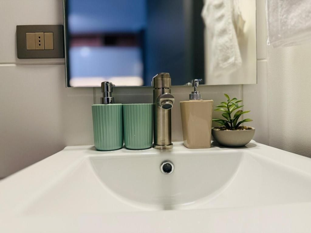 Un lavamanos de baño con un espejo encima, un interruptor de luz y una planta en maceta.