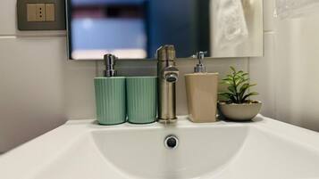 Un lavamanos de baño con un espejo encima, un interruptor de luz y una planta en maceta.