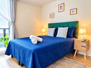 A hotel room with a large bed, two bedside tables, a green upholstered headboard, and a view of the outdoors. - El mejor lugar - Estacionamiento - Wi-Fi (Santiago)