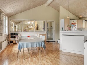 Un comedor amplio con una mesa larga, sillas de madera y una cocina con armarios blancos y una encimera.