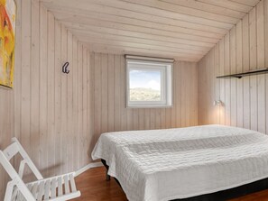 Ein Schlafzimmer mit einem Einzelbett, einem Fenster, einem weißen Stuhl und einer Holzbalkendecke.