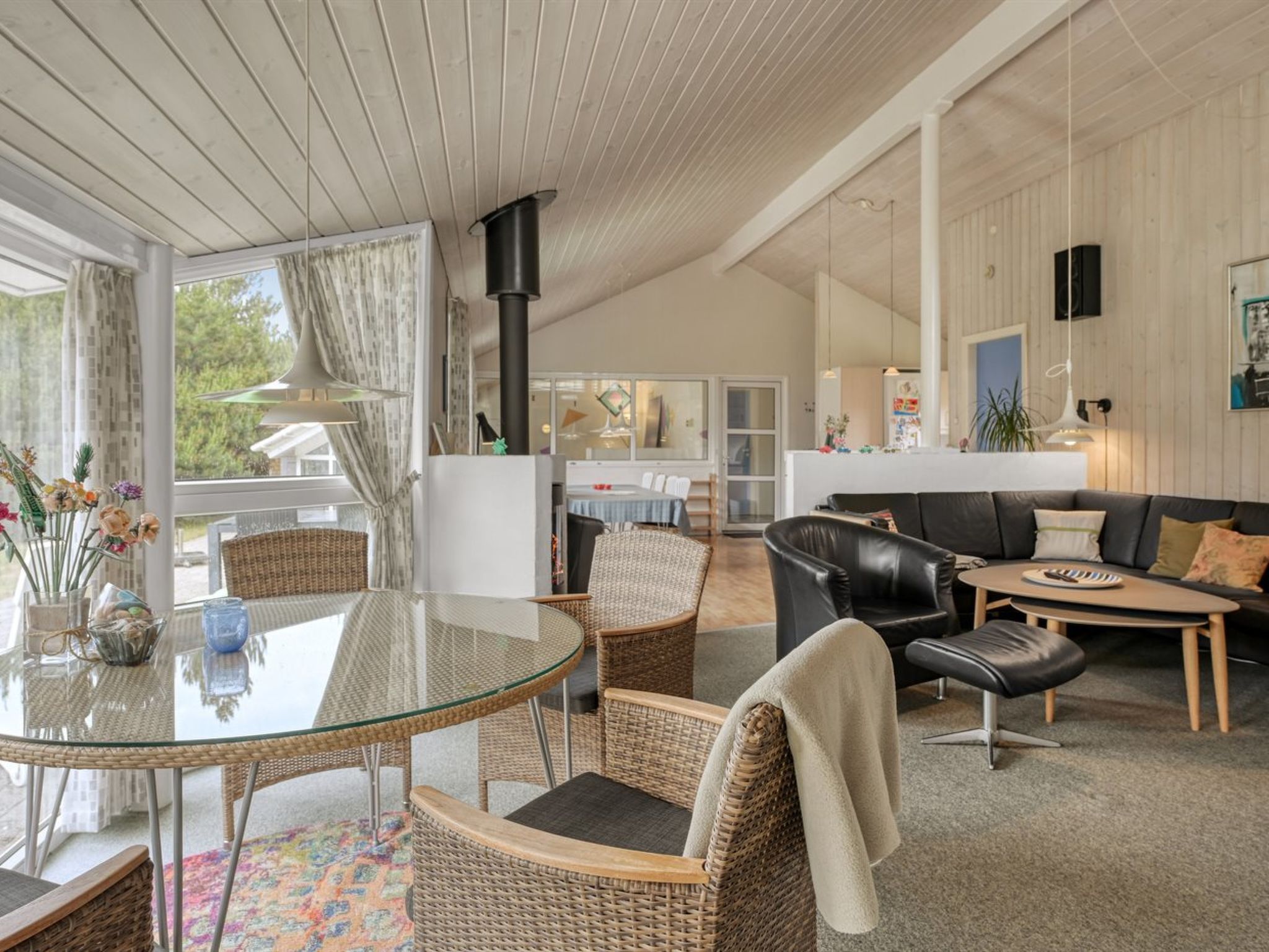 Een moderne woonkamer met een glazen eettafel, rieten stoelen, een leren bank en een salontafel.