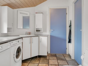Cocina compacta con lavadora, armarios, una encimera y una puerta que da a otra habitación.