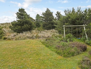 Un campo cubierto de hierba con un parque infantil de madera y árboles frondosos al fondo.