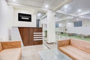 A reception area with a sign reading 'TOWNHOUSE Company Serviced,' a wooden reception desk, two sofas, a glass table, and a view through a glass wall. - Super Townhouse Subhash Chowk (Gurugram)