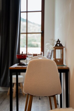 A dining area with a table set for two, a chair, and a view through a window. - Le Petit Chalet: 2-person vacation rental with spa access (AUBURE)