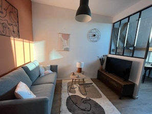 Ein modernes Wohnzimmer mit einer Couch, einem Couchtisch, einem Fernseher und einem großen Fenster.